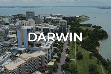 Aerial view of Darwin highlights city buildings, lush parkland, and a shimmering body of water under a cloudy sky. The text 'DARWIN' stands out, capturing the city's vibrant essence and opportunities, including potential business for sale in this thriving locale.